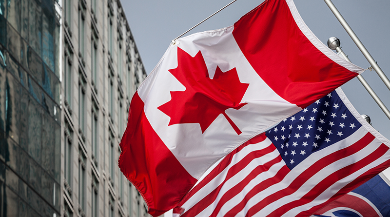 Canadian and US flags with stacked intermodal shipping containers in the background